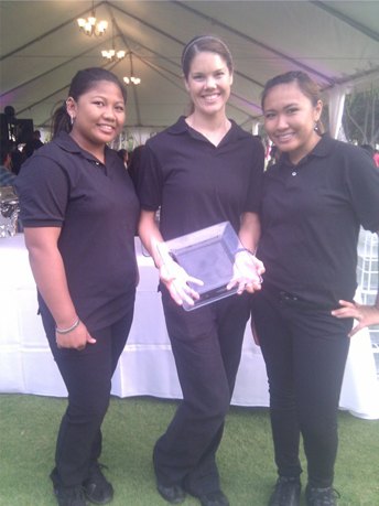 Three Keneke's servers in black polo shirts under a wedding tent